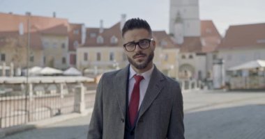 Yakışıklı iş adamı etrafa bakıyor, gözlük takıyor ve dışarıda poz veriyor.