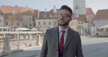 Gözlük takan seksi, zarif iş adamı. Etrafa bakıyor, ortaçağ şehir geçmişinin önünde dönüp gidiyor.