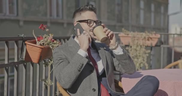 Borotválatlan Fiatalember Hosszú Kabátban Telefonál Asztalhoz Kávét Iszik Félrenéz Mosolyog — Stock videók
