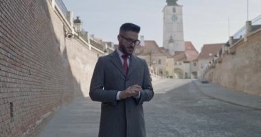 Genç yakışıklı iş adamı avuçlarını ovuyor, paltosunu düzenliyor, gözlük takıyor.