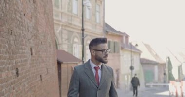Genç ve seksi iş adamı takım elbise ve uzun palto giyiyor, gözlükleri tamir ediyor, yan çizip uzaklaşmaya çalışıyor.