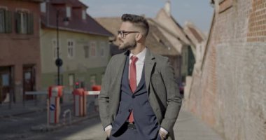 Seksi iş adamı ellerini ceplerine sokuyor, gözlüklerini ayarlıyor, ceketini düzenliyor ve gülümsüyor.