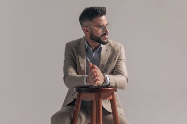Ciddi bir iş adamı avuçlarını ovalıyor ve gri arka planda oturuyor.