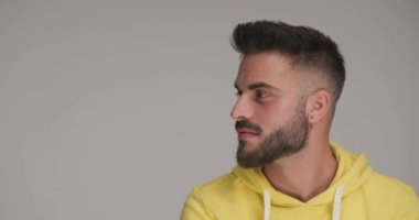 Sarı kapüşonlu sakallı mutlu bir genç stüdyoda gri arka plana bakıp gülümsüyor.