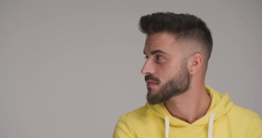 Tıraşsız, genç ve çekici bir adam. Stüdyoda gri arka planda sırıtıyor. Sarı kapüşonlu.