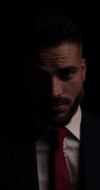 Takım elbiseli gizemli iş adamı avuçlarını ovuyor, kendinden emin ve seksi ve dramatik karanlık bir arka planda poz veriyor.