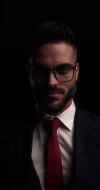 Takım elbiseli zarif genç iş adamının portresi. Gözlük ve ceket düzenliyor. Davet ediyor ve karanlıkta kayboluyor.