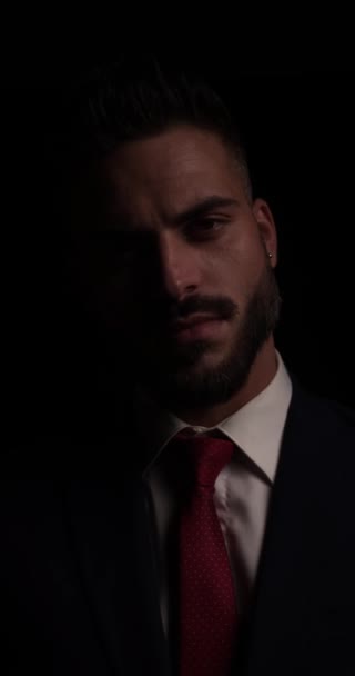 szexi fiatal férfi egy függőleges videó érzékien megható ajkak, beállítása öltöny, séta el és hívogató, miközben halványul a sötétben