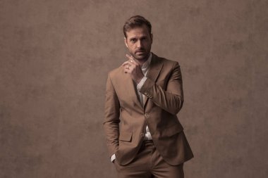 sexy businessman sensually touching his face and holding one hand in pocket against brown background