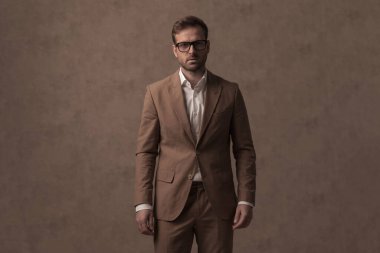 sexy businessman wearing a nice brown suit and eyeglasses in a fashion pose