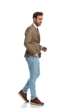 side view of a handsome businessman walking with style and one hand in pocket against white background