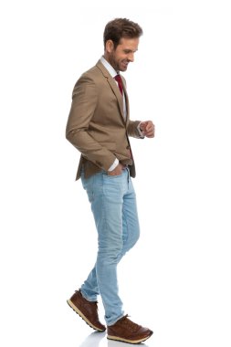 side view of a sexy businessman walking, looking down, smiling and holding one hand in pocket 