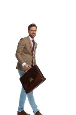 side view of a handsome businessman smiling wide, holding a briefcase and walking against white background