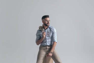 portrait of seated young man looking to side and holding jacket over shoulder on grey background in studio
