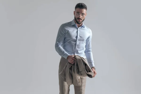 cool young businessman holding jacket in hands and posing on grey background in studio