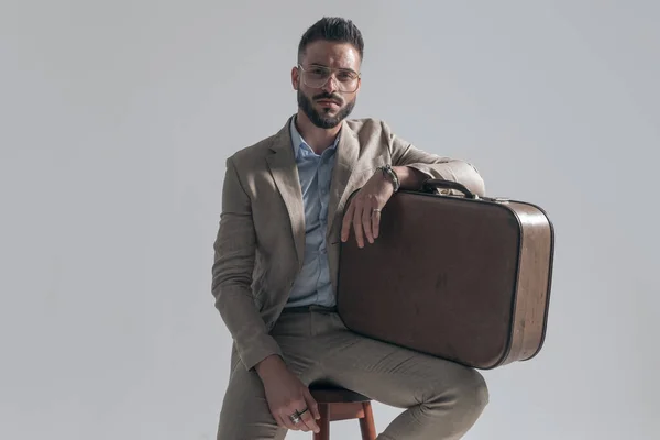 Seated Young Businessman Glasses Holding Arms Suitcase Sitting Grey Background — Fotografia de Stock