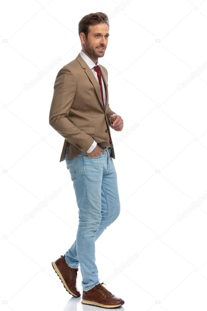 side view of a handsome businessman walking with one hand in pocket and looking away against white background