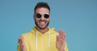 sexy casual man feeling excited, clapping his hands, wearing sunglasses and gesturing good job