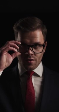 vertical project video of elegant businessman adjusting glasses and tie and smiling while standing a light in studio