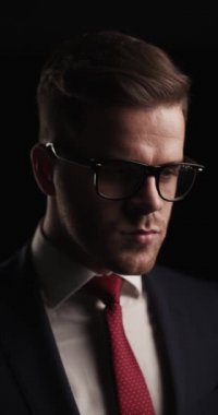 side view of sexy man with glasses looking away, being thoughtful and thinking while standing on black background in studio