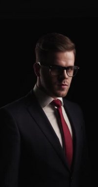 vertical project video of sexy man in elegant suit looking to side, wearing glasses and arranging tie  while walking away in the dark