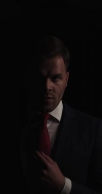 vertical project video of elegant young businessman arranging tie, hair and suit, moving in a back view position and walking away in the dark