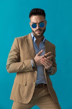 Retro gözlüklü seksi sakallı adam stüdyoda mavi arka planda parmaklarına dokunup okşuyor.