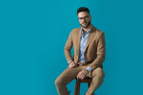 Sedutor Jovem Empresário Segurando Braços Pose Moda Sentado Fundo Azul — Fotografia de Stock