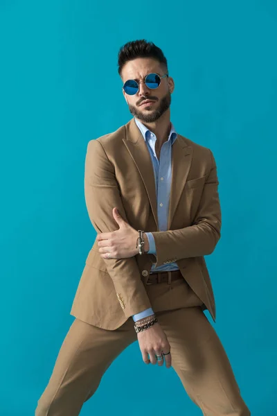 エレガントな剃毛されていない若いです男でレトロサングラスは ファッション方法で肘に触れ 自信を持って青の背景にスタジオでポーズ — ストック写真