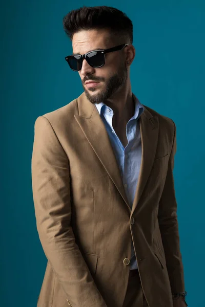 在演播室里 戴眼镜的性感大胡子男人带着蓝色背景 带着自信的样子站在一边摆姿势 — 图库照片