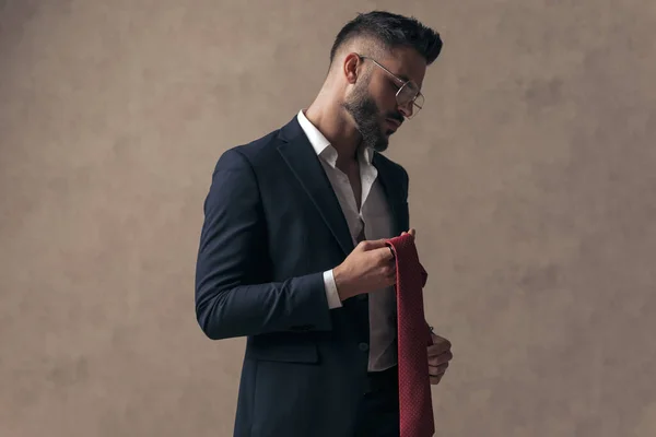 side view of a cool businessman holding his tie and wearing eyeglasses against wallpaper