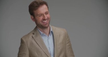 Zeki sıradan iş adamı gülümsüyor, aşağı bakıyor, yakasını gri arka planda onarıyor.