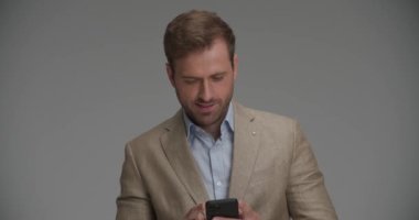 Yakışıklı iş adamı telefonuna mesaj yazıyor ve gri arka plandaki kamerayı işaret ediyor.