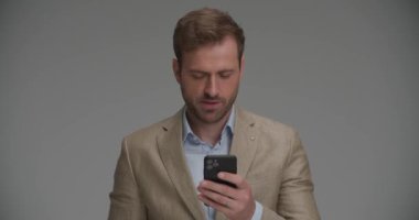 Telefonuna yazı yazıp kamerayı işaret eden yakışıklı bir iş adamı.