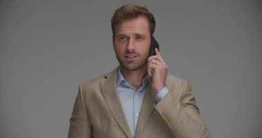 Genç yakışıklı iş adamı cep telefonuyla konuşuyor sonra da kameraya gülümsüyor.