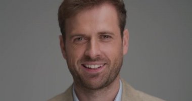 Gri arka planda kameraya gülümseyen yakışıklı bir iş adamına yaklaş.