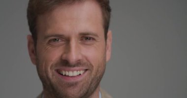 Geniş gülümseyen ve gri arka planda mutlu hisseden genç bir iş adamına yaklaş.