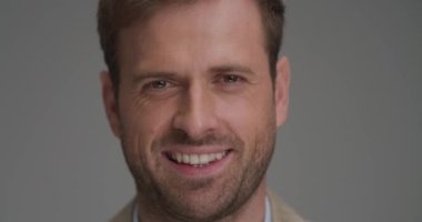 Gri arka planda kameraya gülümseyen mutlu bir iş adamına yaklaş.