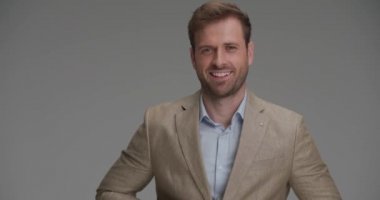 Seksi model takım elbisesini kapatıyor ve gri arka planda kameraya gülümsüyor.