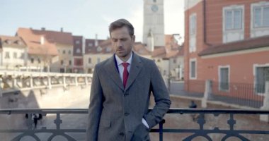 Yakışıklı iş adamı bir eli cebinde çitlere yaslanıyor ve kameraya bakıyor.