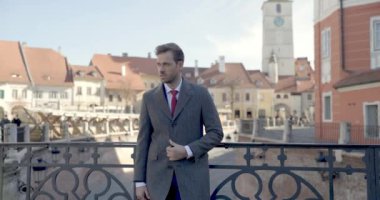 Çekici iş adamı çantasını tutuyor, paltosunu tamir ediyor, başka tarafa bakıyor ve baş parmağını kaldırıyor.