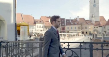 Transilvanya 'nın ortaçağdan kalma bir kasabasındaki köprüde yürüyen takım elbiseli şık bir işadamının yan görünüşü.