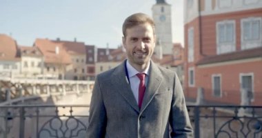 Gülümseyen iş adamı kameraya doğru yürüyor, takım elbisesini tamir ediyor.