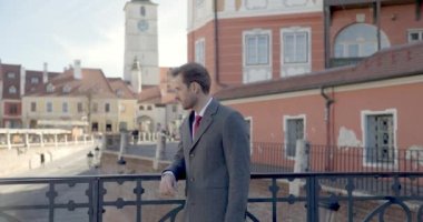 Yakışıklı iş adamı köprüde el ele tutuşur, yan yana bakar, şehre hayran olur, yüzüne dokunur ve kamera yakınlaşırken gülümser.