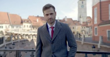 Orta Çağ 'ın arka planında şık takım elbiseli çekici sakallı bir adamın portresi. El ele tutuşup poz veriyor, kamera yaklaşırken hafifçe gülümsüyor.