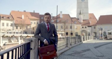 Seçkin bir iş adamının bavuluyla ortaçağ arka planında dalgın dalgın dalgın baktığı bir video projesi.