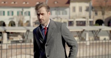 Yakışıklı iş adamı güneşin altında dikiliyor, aşağı bakıyor, ceketini tamir ediyor.