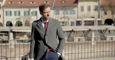 Proje videosu, takım elbiseli, çantayla aşağı bakan, el ele tutuşan, yana bakan, yürüyen, kamerayı yakınlaştırırken başka yöne bakan çekici sakallı adamın videosu.