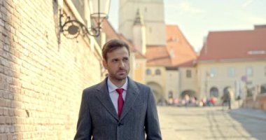 Yakışıklı iş adamı duvarın yanında yürüyor, gülümsüyor, paltosunu tamir ediyor ve dışarıda eğleniyor.