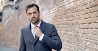 Manken kravatını düzeltiyor ve yüzünde kocaman bir gülümsemeyle ceketini düzeltiyor.